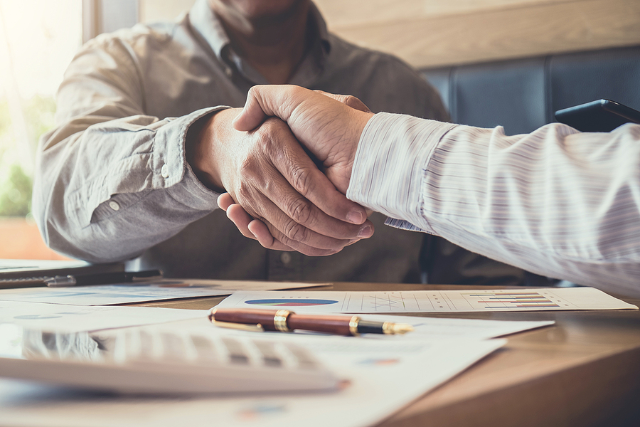 Two people shake hands over a desk in an office.