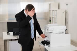 Irritated businessman looking at paper stuck in printer at office