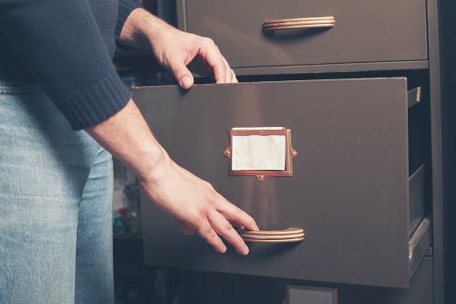 A person is opening a drawer in a brown filing cabinet.