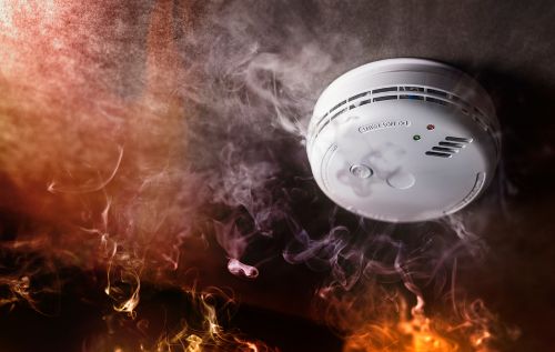Fire and smoke are swirling up around a smoke detector.