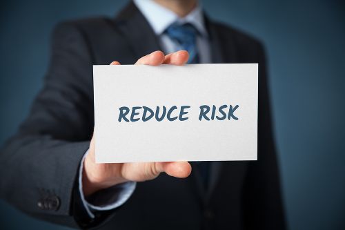 A person in a business suit holds up a white card with the words REDUCE RISK.