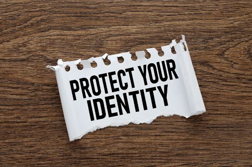 The words PROTECT YOUR IDENTITY are printed on a piece of paper that is torn and laying on a wood surface.